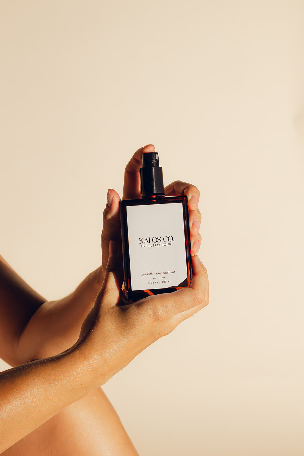 someone holding amber spray bottle with white label that says kalos co hydra face tonic