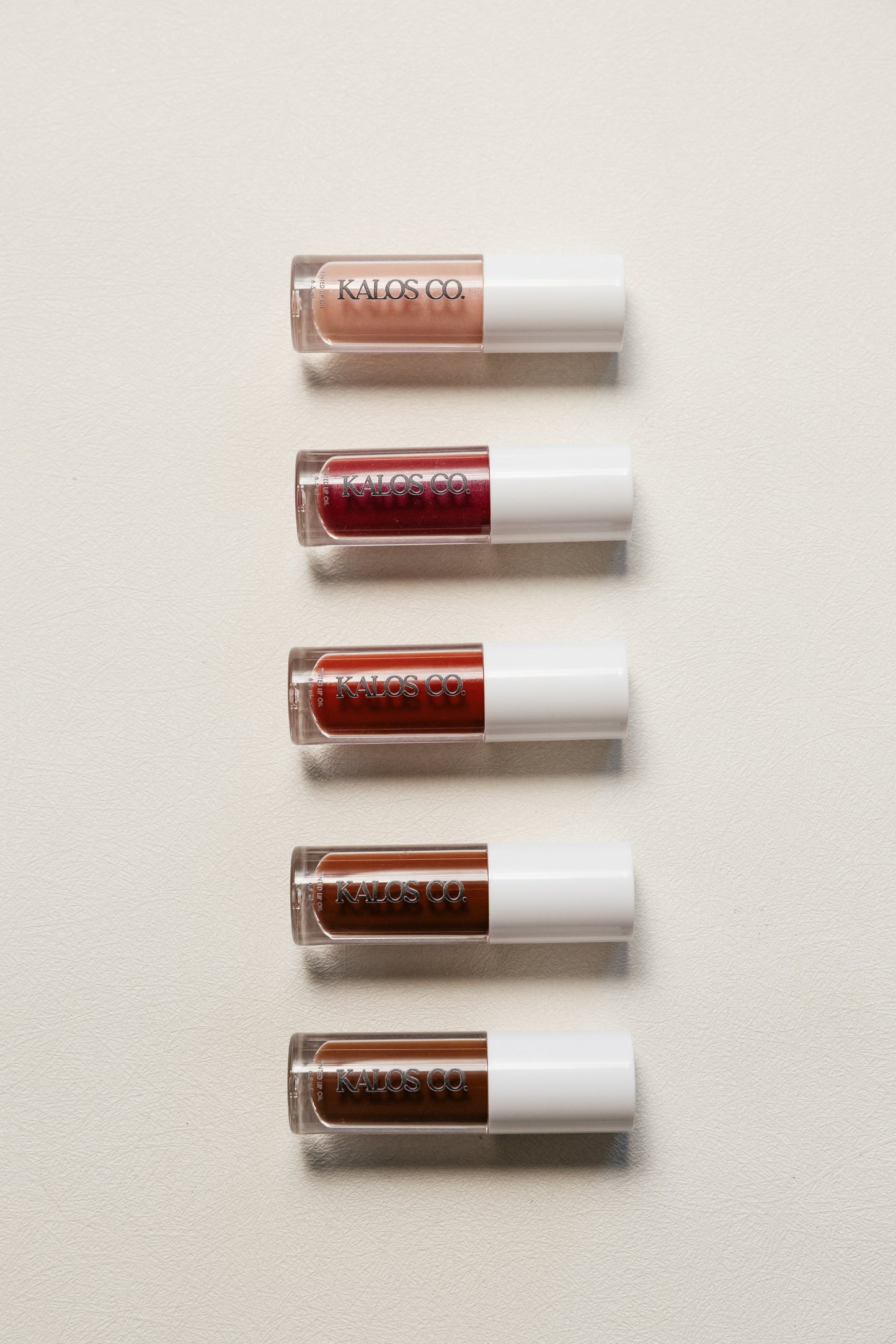 5 lip gloss tubes from Kaloo on a light beige background