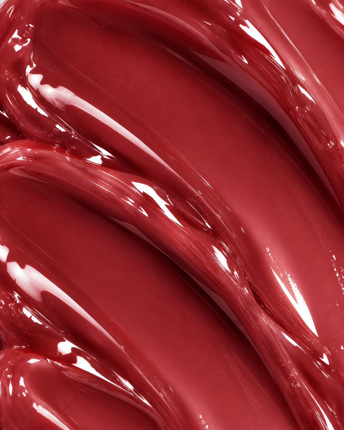A close-up of glossy, thick red cosmetic cream or liquid swirled in smooth, curved strokes with reflective highlights.