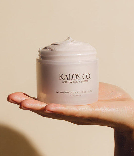 Hand holding a jar of Kalos Co. cream against a neutral background