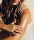 Woman applying sunscreen to her arm with a beige background