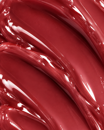 A close-up of glossy, thick red cosmetic cream or liquid swirled in smooth, curved strokes with reflective highlights.