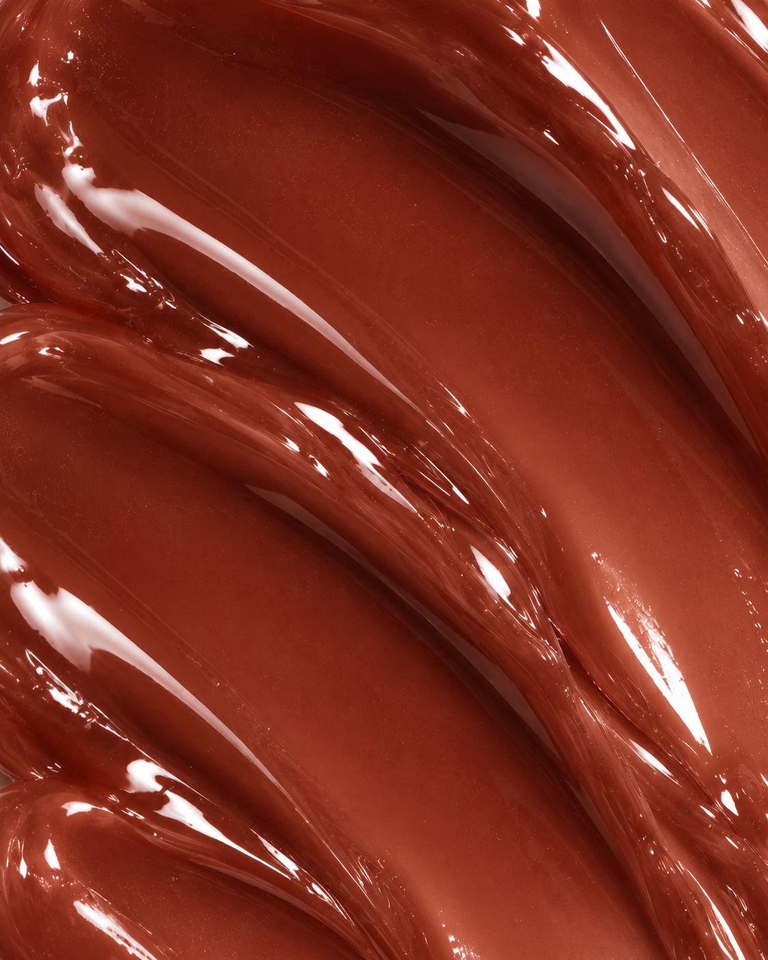 A close-up texture shot of a glossy, thick brown cosmetic cream or liquid swatch, showing smooth, flowing layers with a high-shine reflective finish.